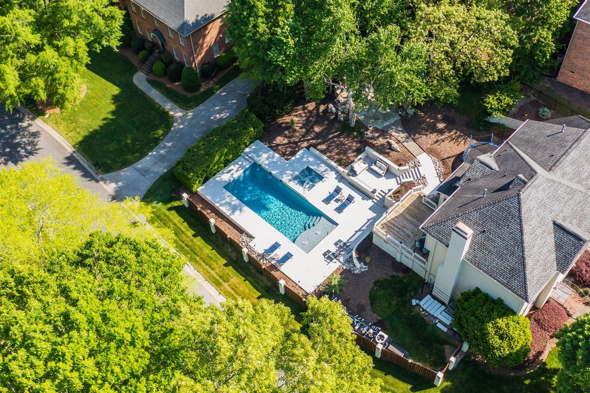 Aerial view of a backyard pool beside a house, surrounded by trees and patio seating