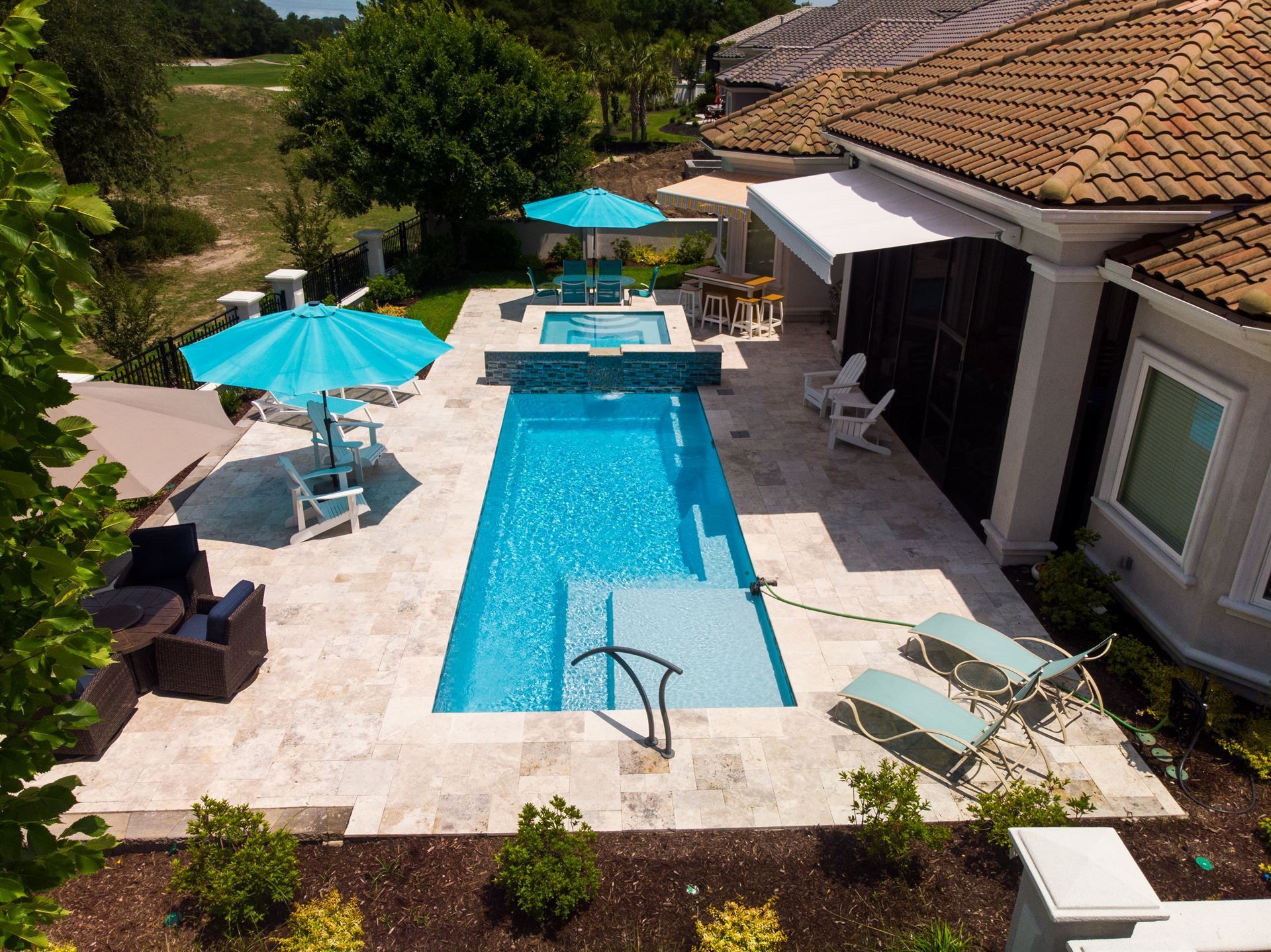 Backyard pool with turquoise umbrellas, lounge chairs, and a tiled patio beside a house