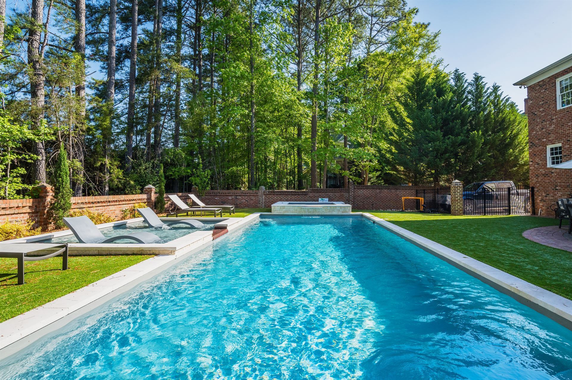 Backyard pool with blue water, lounge chairs, and tall trees beside a brick house
