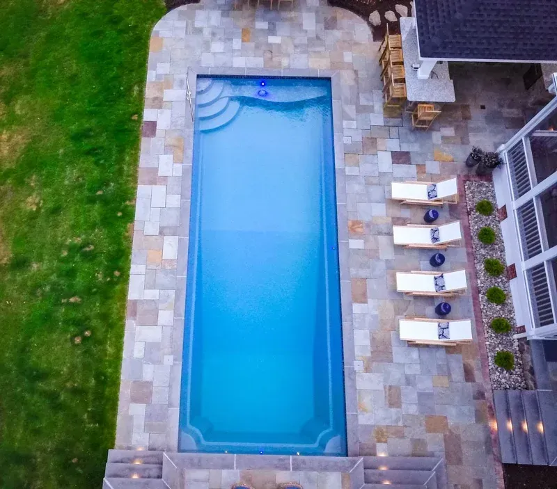 Aerial view of a rectangular blue pool with stone patio, lounge chairs, and green lawn
