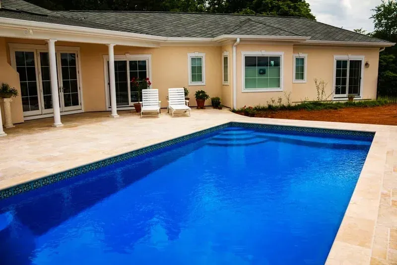 Backyard swimming pool beside a beige house with patio and lounge chairs