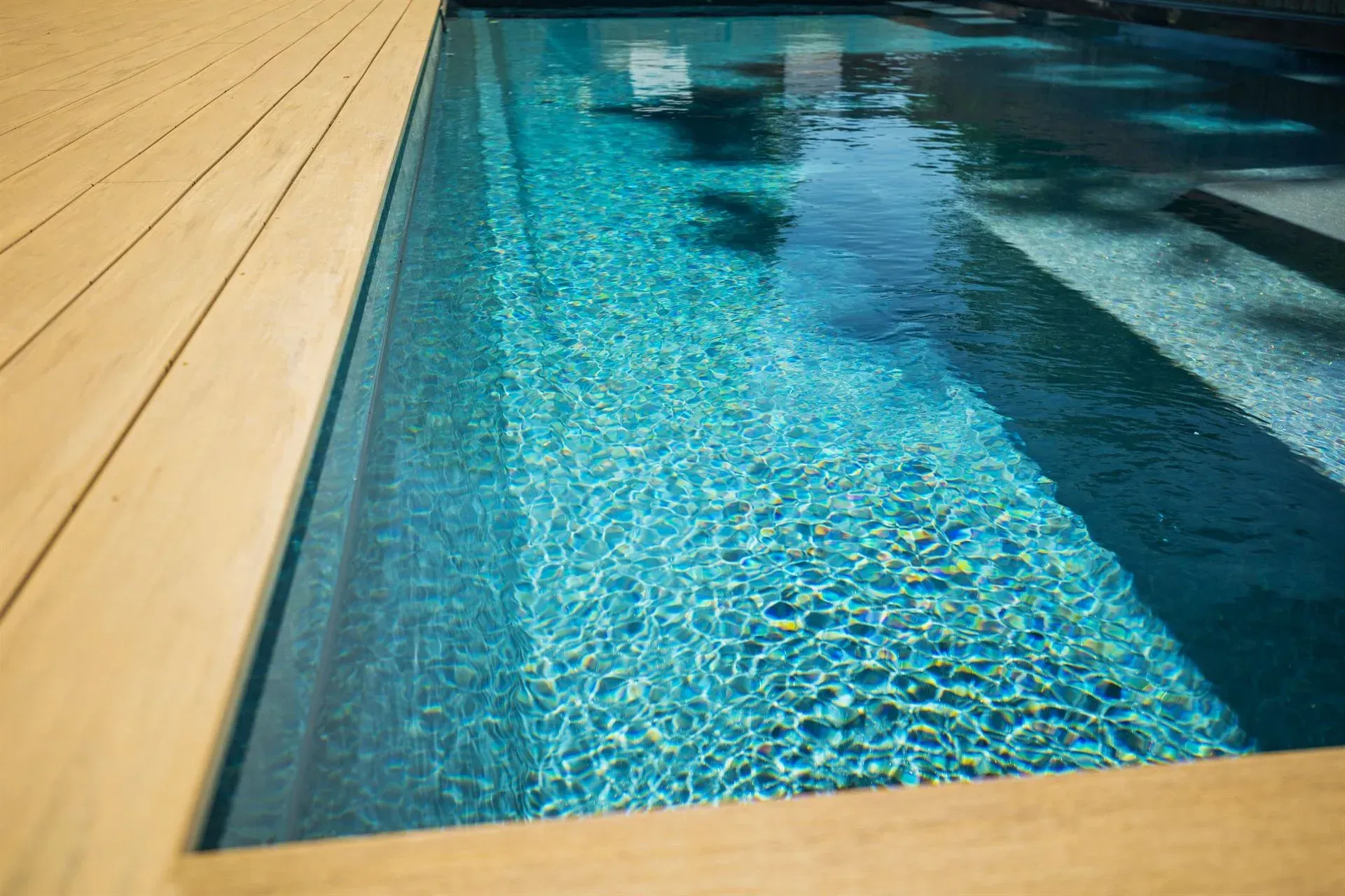 Modern pool with turquoise water beside a light wooden deck