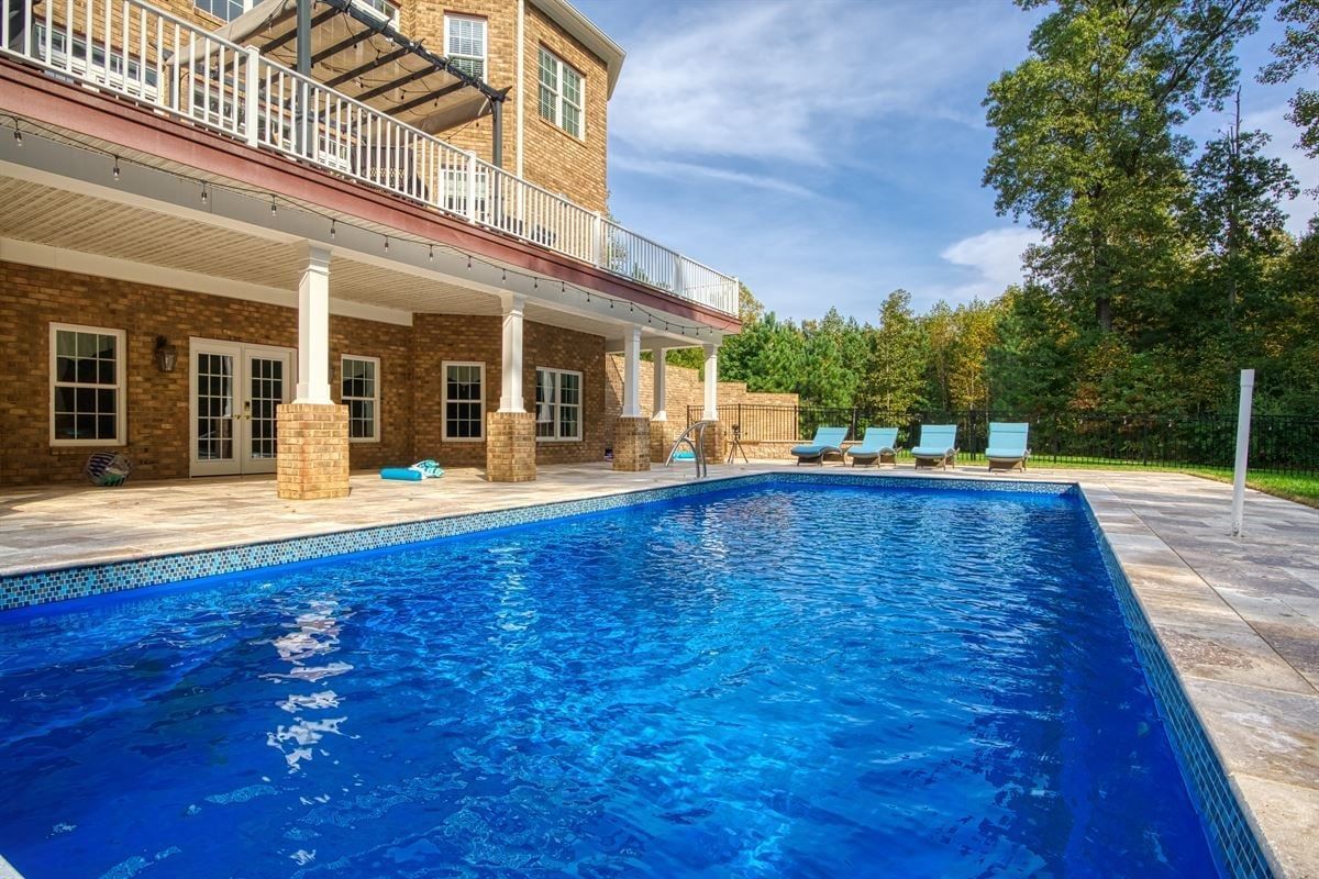 Luxury home patio with blue swimming pool, lounge chairs, and stone terrace under a bright sky