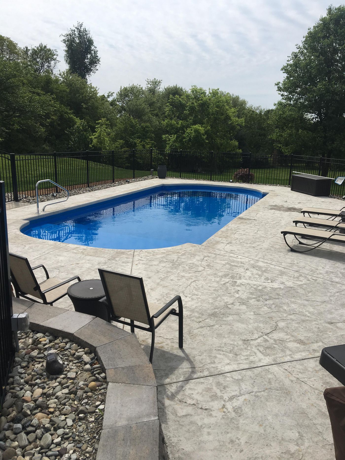 Outdoor swimming pool with blue water, stone patio, lounge chairs, and trees surrounding it