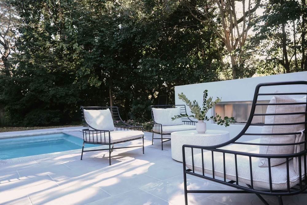 Modern patio with white chairs, a low table, and trees in the background
