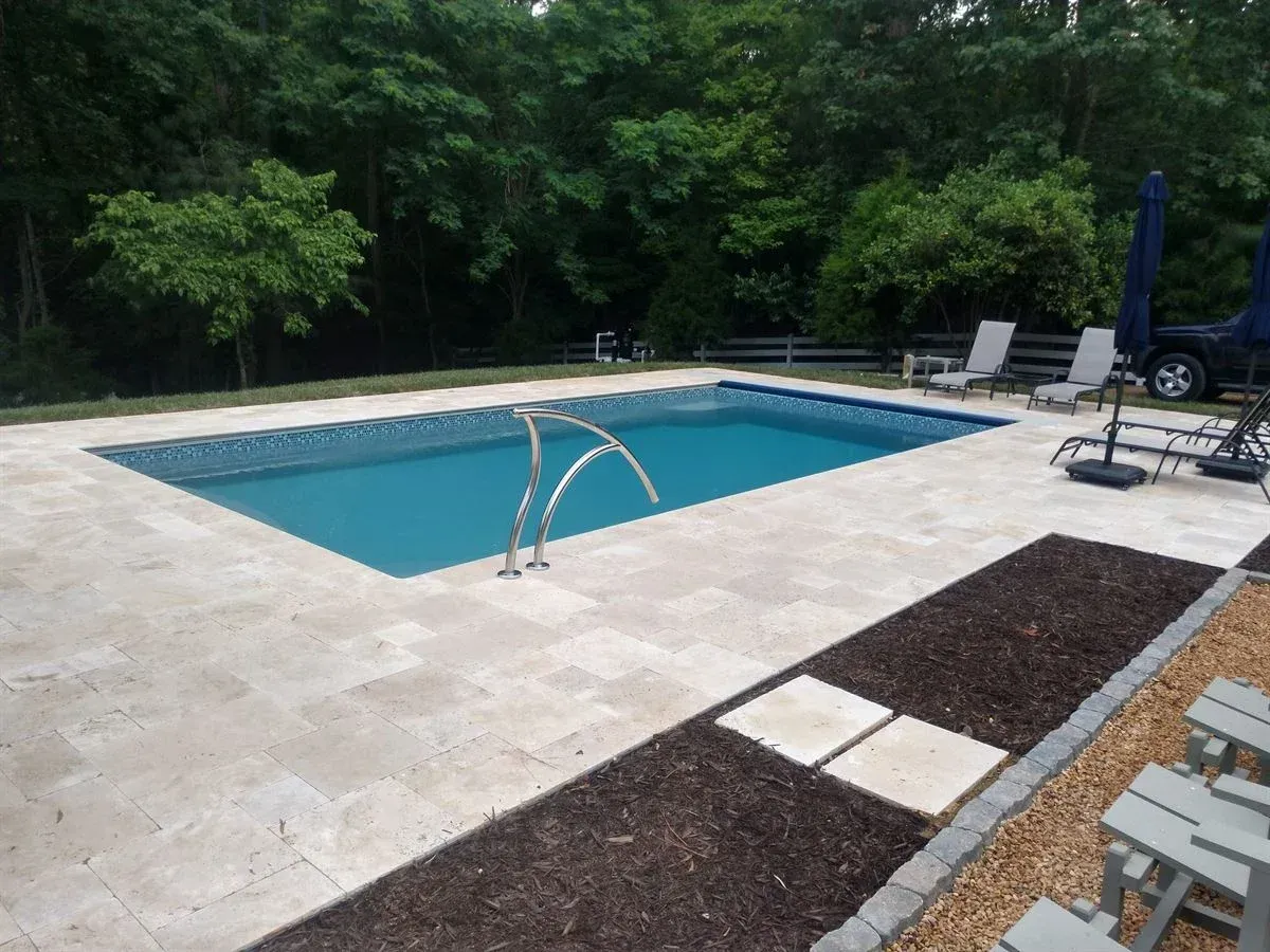 Backyard swimming pool with stone patio, lounge chairs, and surrounding trees