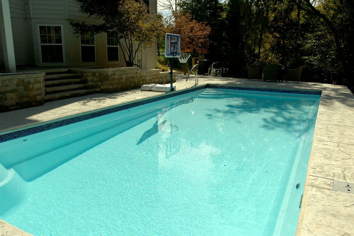 Outdoor swimming pool with clear turquoise water beside a stone deck and house