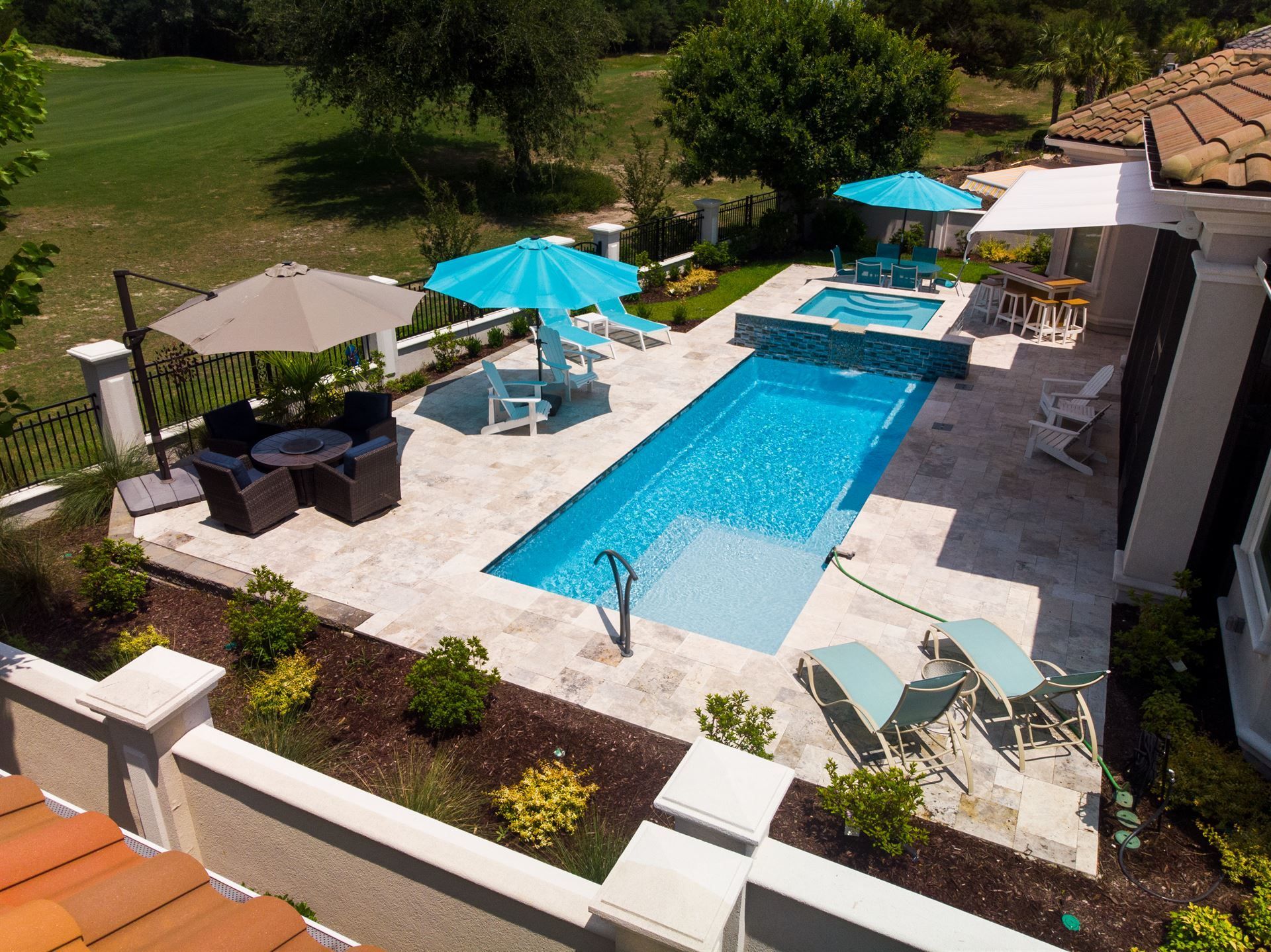Backyard pool with blue umbrellas, patio seating, and white lounge chairs in bright sunlight