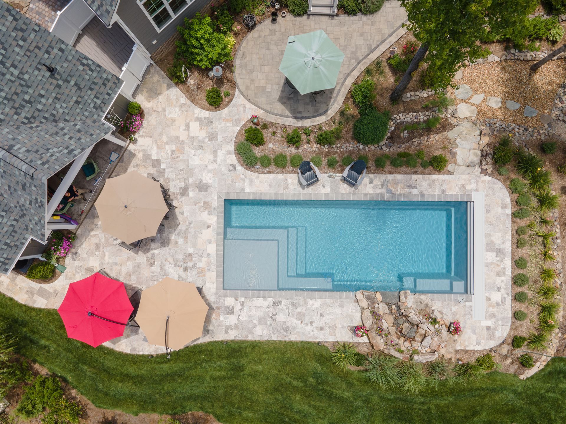 Aerial view of a backyard pool with patio furniture, umbrellas, and landscaped garden areas.
