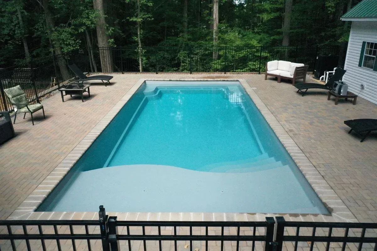 Backyard pool with blue water, tan deck, lounge chairs, and forested surroundings