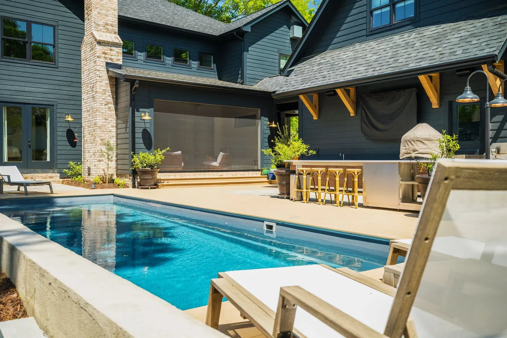 Backyard pool beside a dark stone house with lounge chairs and patio seating