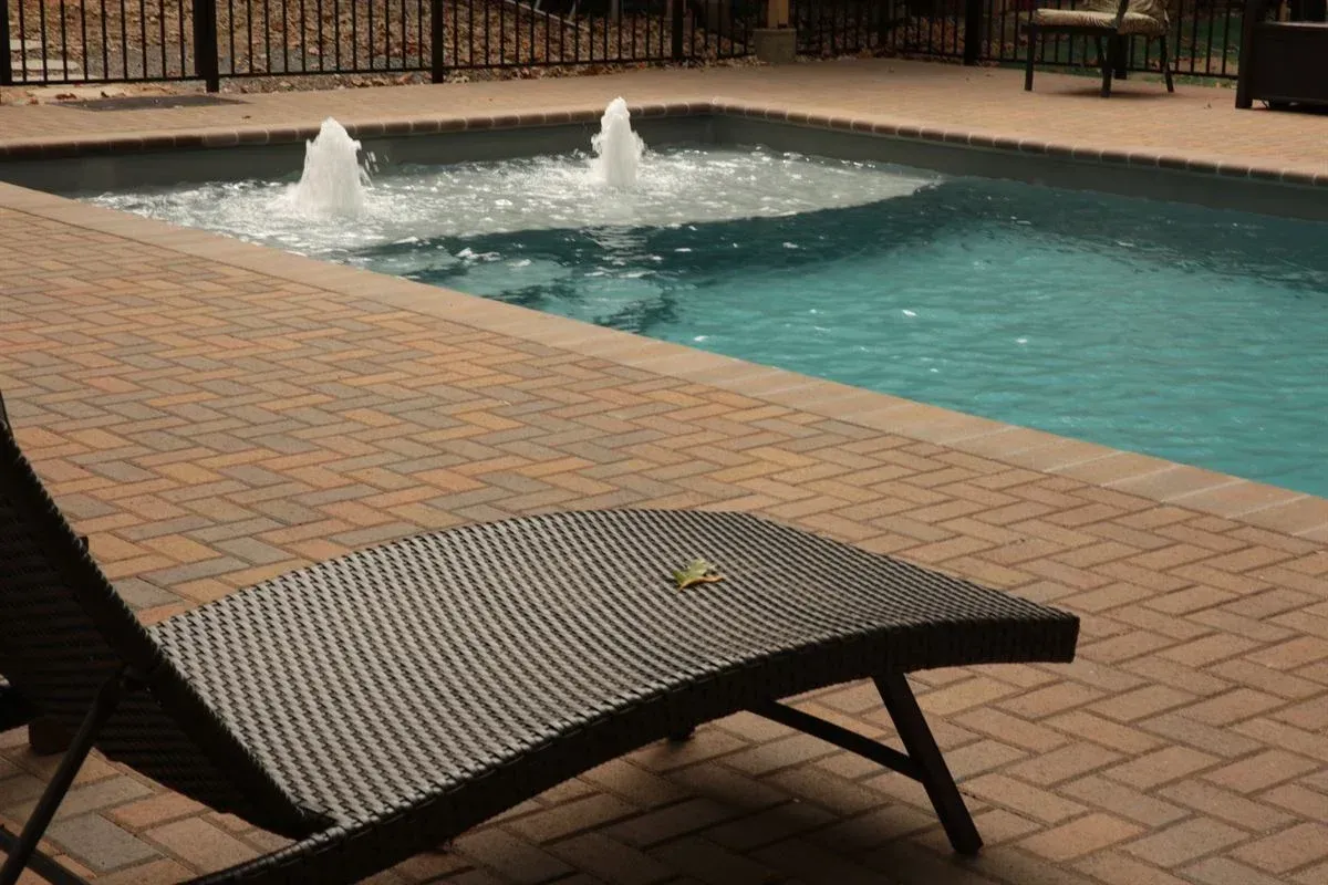Lounge chair beside a turquoise pool with fountains and brick patio tiles