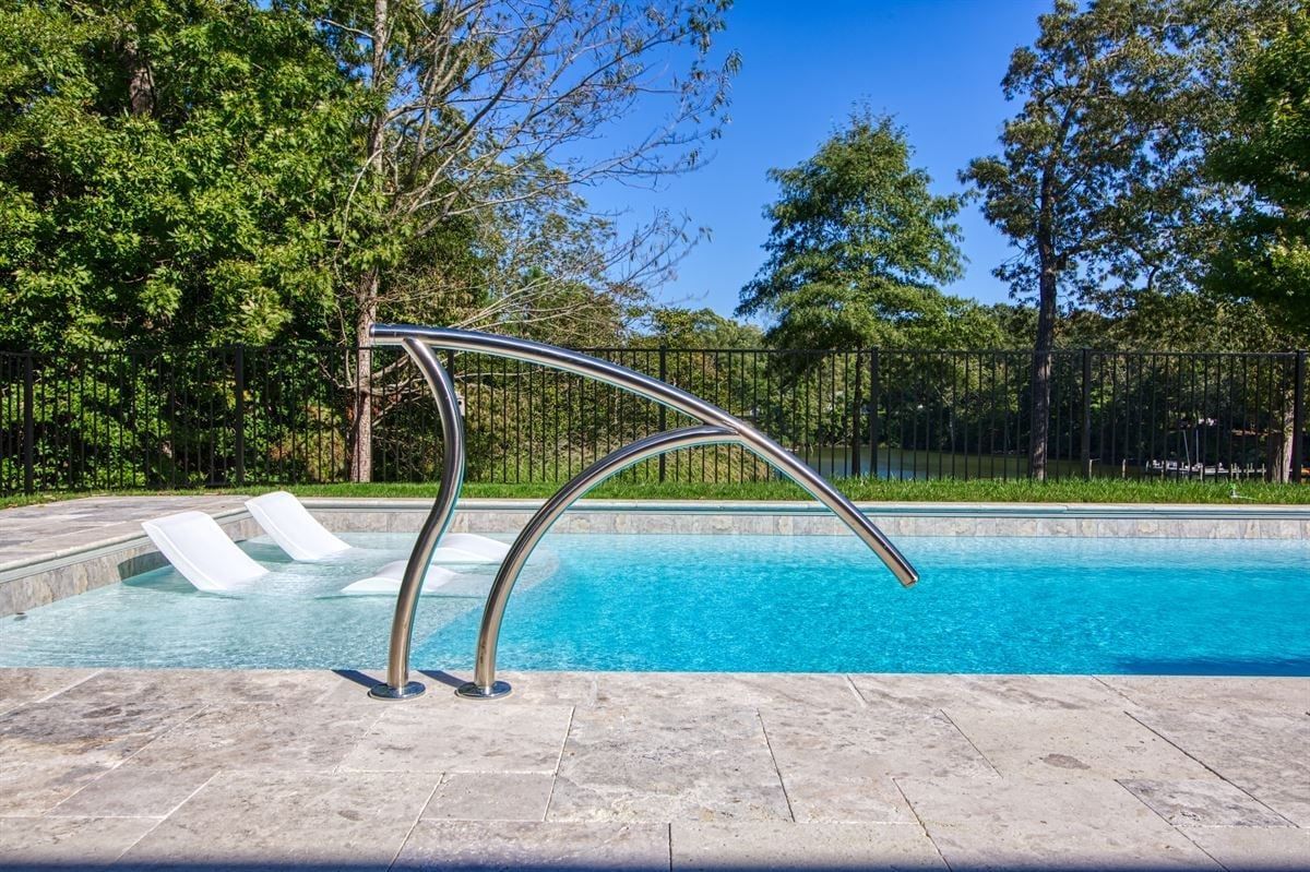 Outdoor pool with a stainless-steel waterfall arch and lounge chairs beside a bright blue pool.