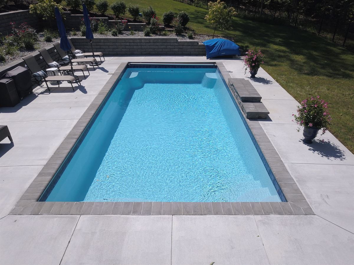 Rectangular backyard swimming pool with blue water, surrounded by a light stone patio and lounge chairs.