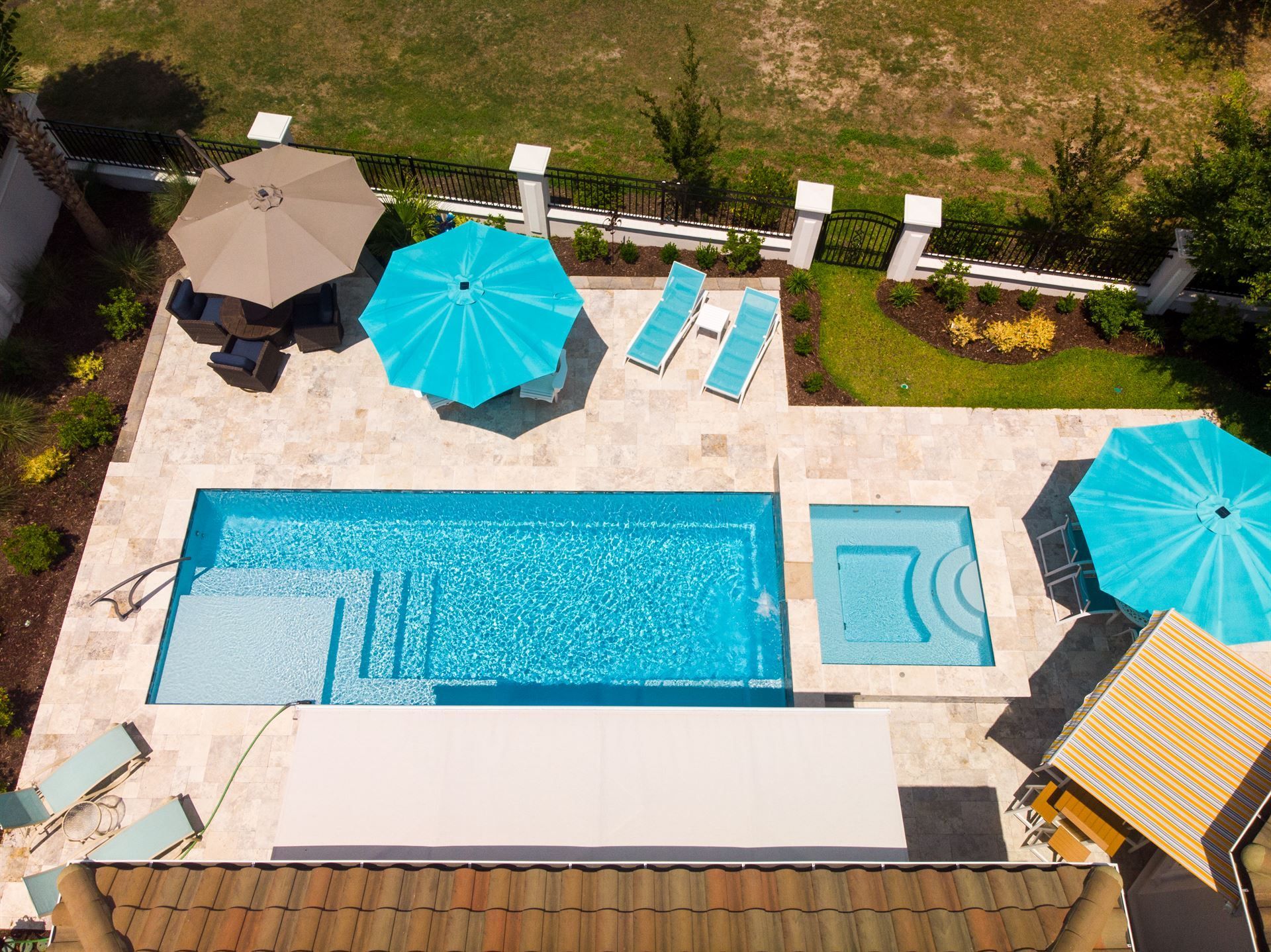 Overhead view of a backyard pool with turquoise umbrellas, lounge chairs, and a spa area