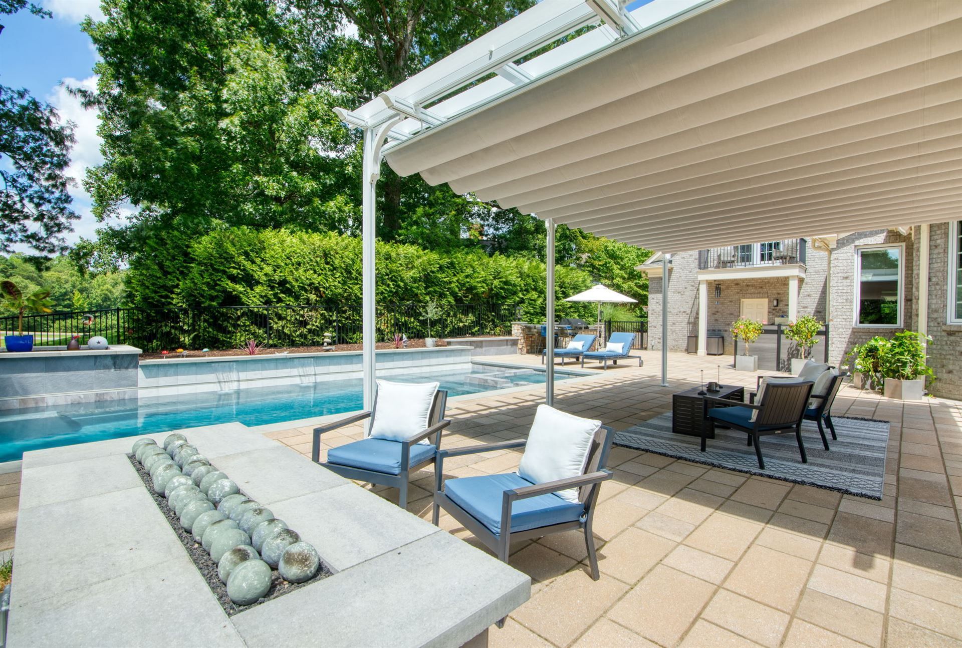 Patio lounge beside a backyard pool with covered seating, blue cushions, and a fire pit table