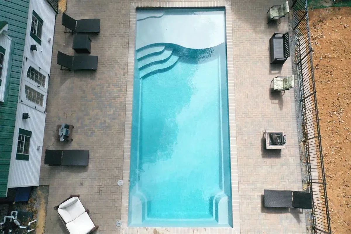 Aerial view of a rectangular turquoise pool surrounded by lounge chairs on a paved patio.