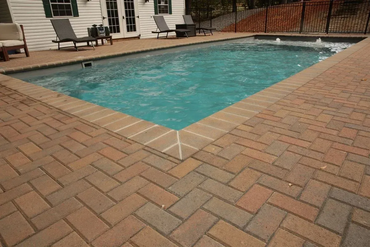 Backyard swimming pool with turquoise water, surrounded by tan brick patio and lounge chairs