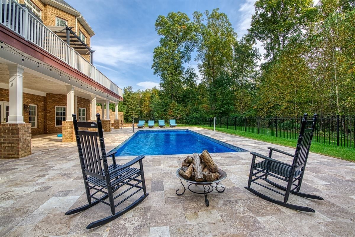 Backyard patio with black rockers facing a blue swimming pool beside a large house