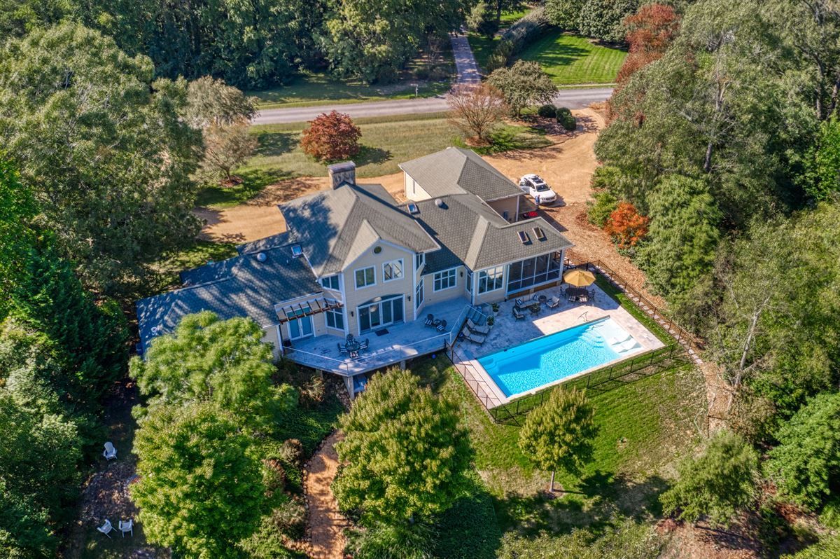 Aerial view of a large gray house with a blue backyard pool surrounded by dense trees.