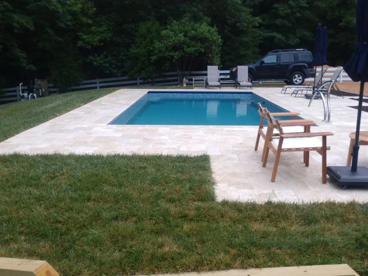 Backyard swimming pool with white patio, lawn, chairs, and a parked SUV in the background