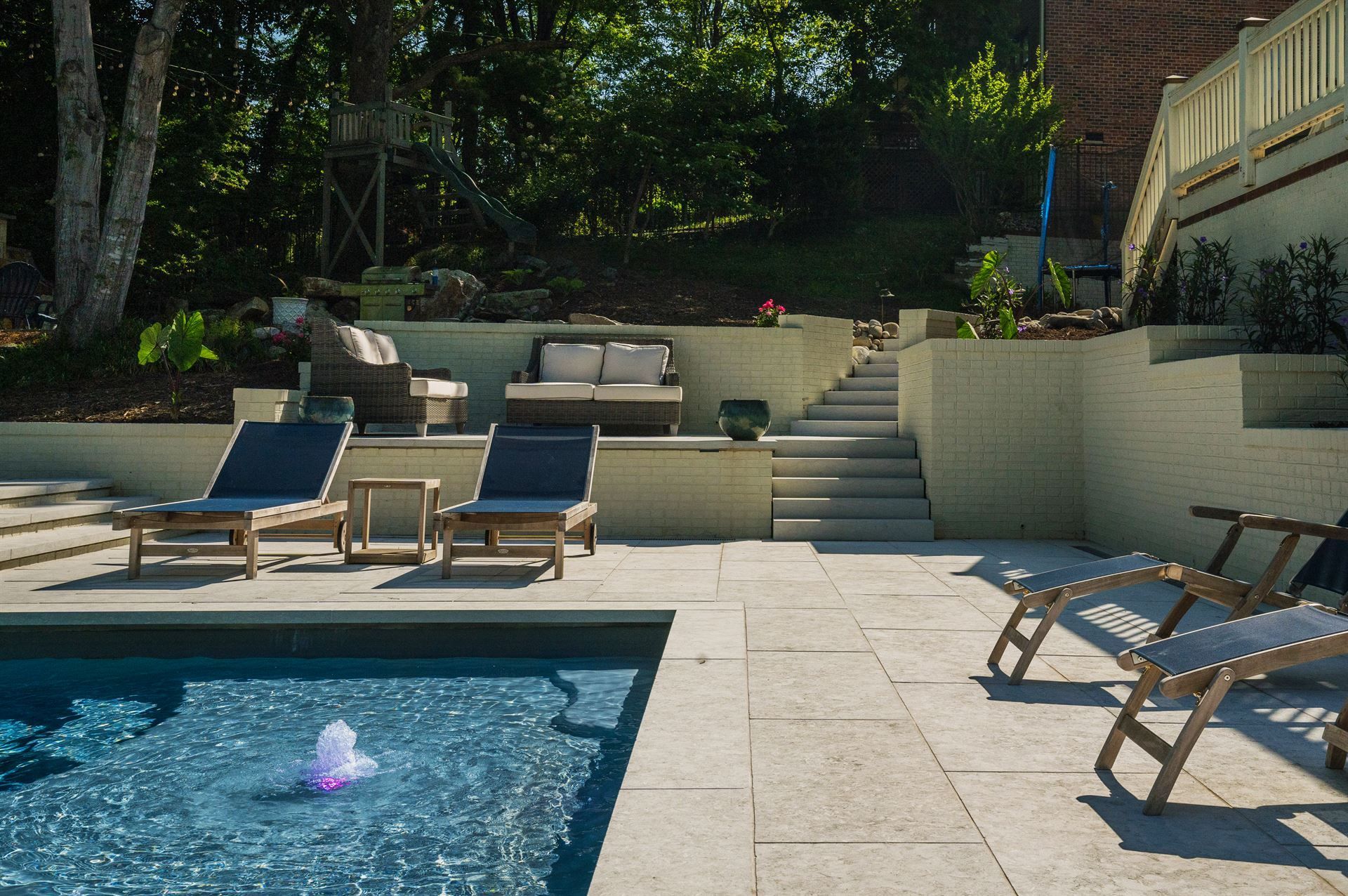 Backyard pool with lounge chairs, stone patio, and raised garden seating area in sunlight