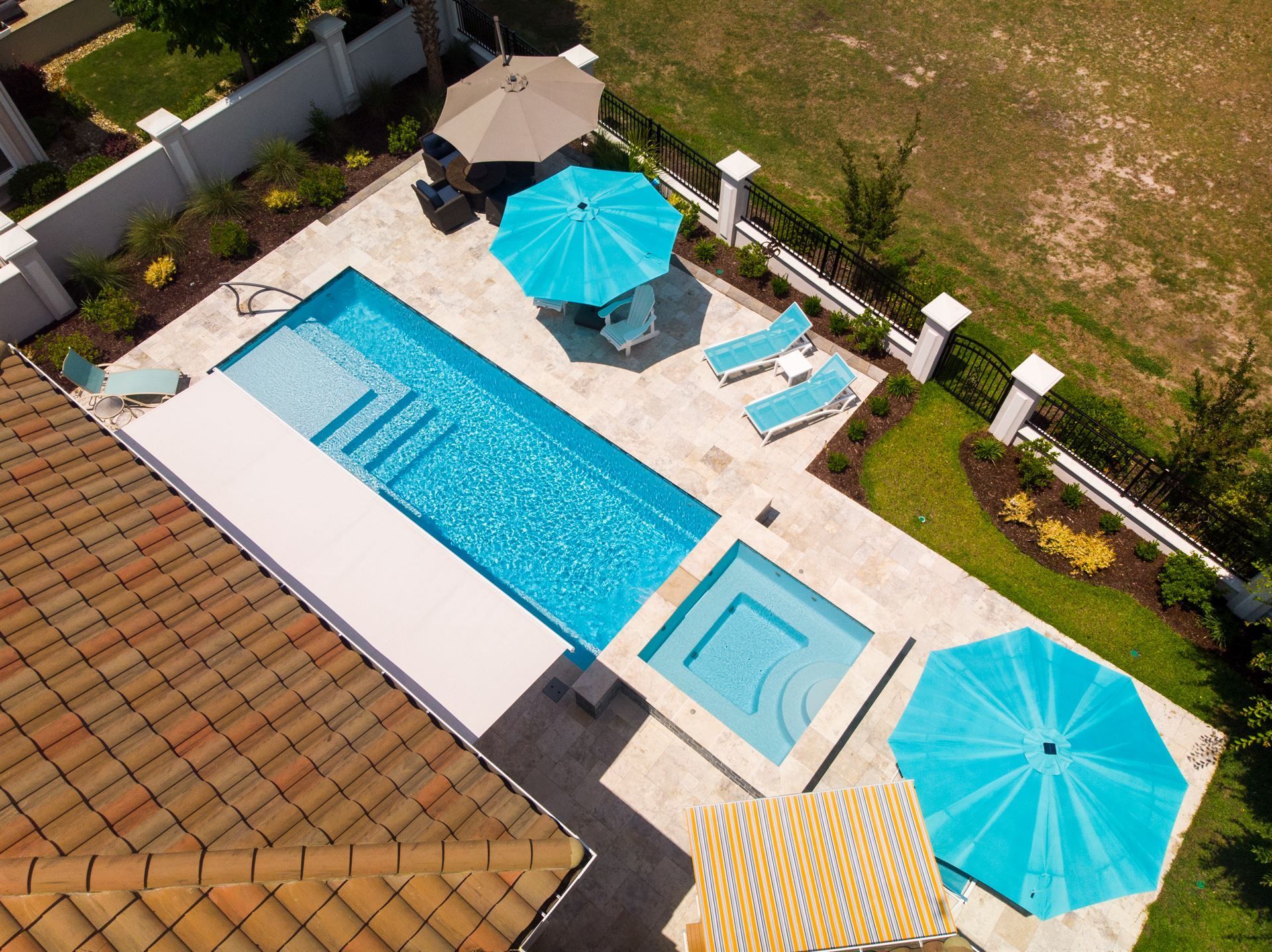 Aerial view of a backyard pool with blue umbrellas, lounge chairs, and a tiled patio