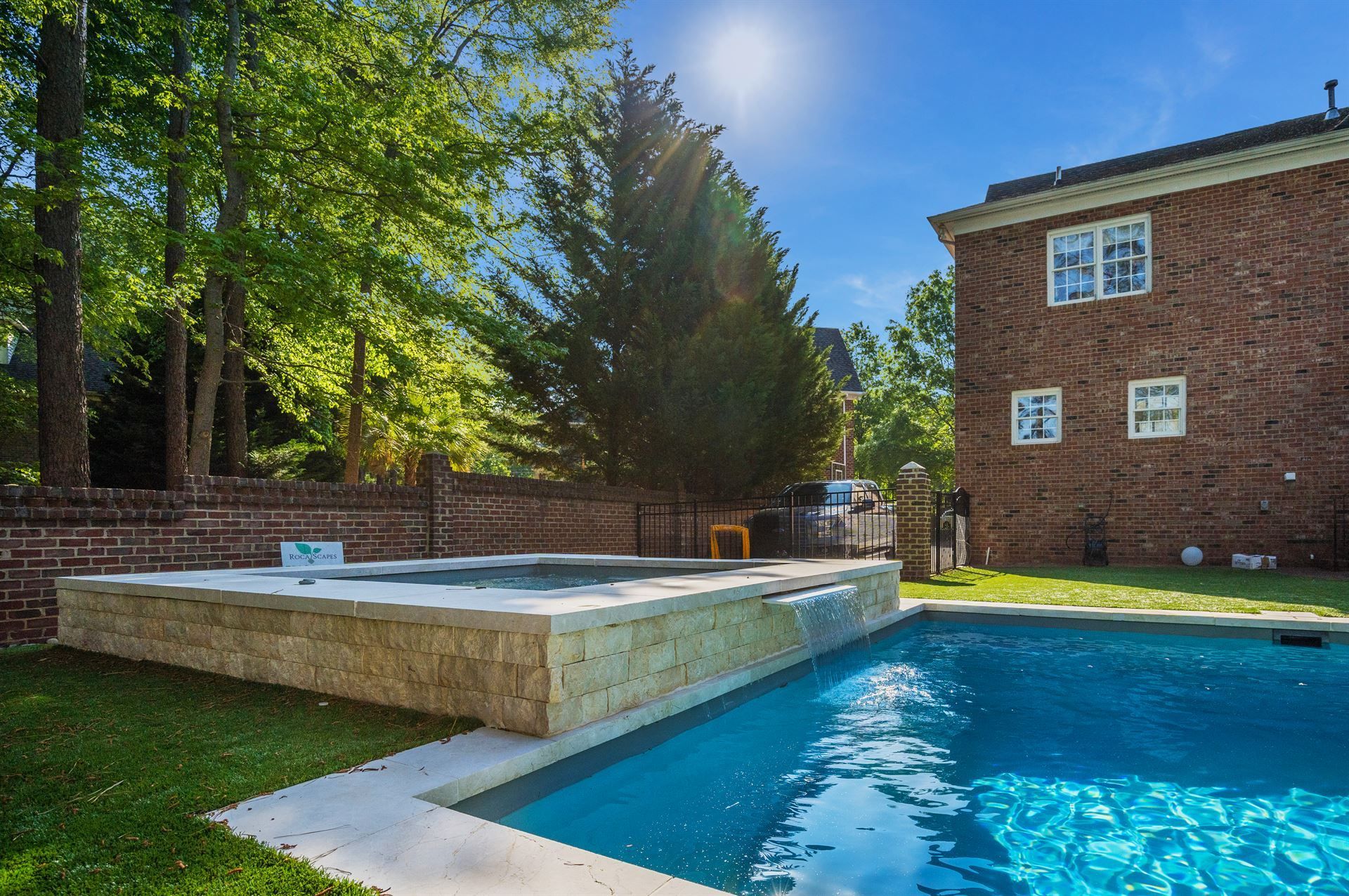 Backyard pool beside a stone hot tub and brick house on a sunny day