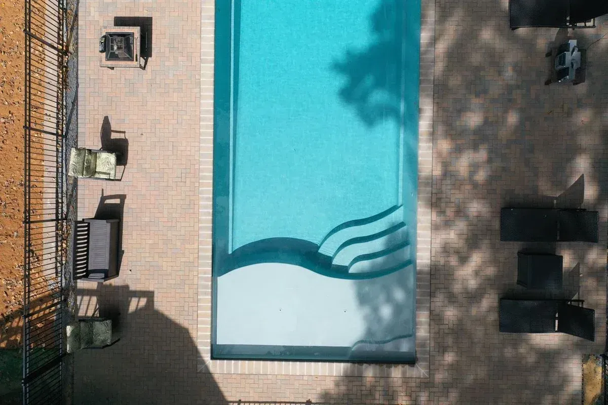 Overhead view of a rectangular swimming pool beside a patio with lounge chairs and tables.