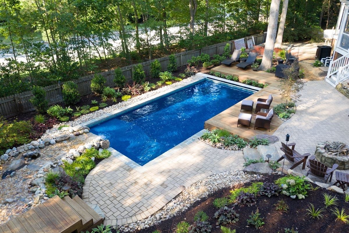 Backyard pool with blue water, stone patio, lounge chairs, and surrounding trees and landscaping