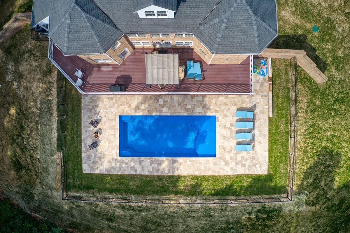 Aerial view of a backyard with a blue swimming pool, patio deck, lounge chairs, and a house.
