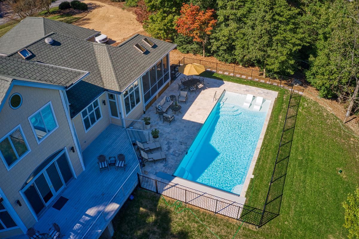 Aerial view of a house with a backyard patio and a long rectangular swimming pool enclosed by a fence.