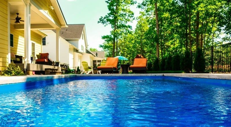 Backyard pool beside a house with lounge chairs and trees on a sunny day