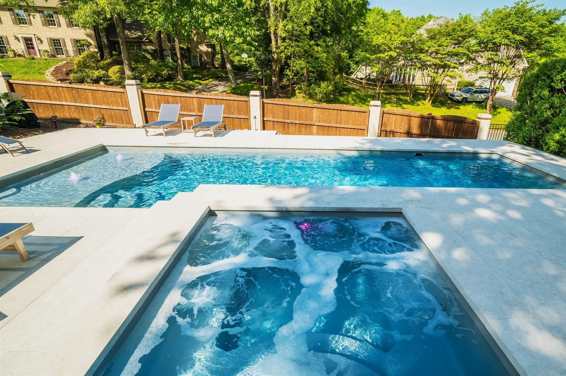Modern backyard pool with blue water, lounge chairs, and lush greenery under bright sunlight