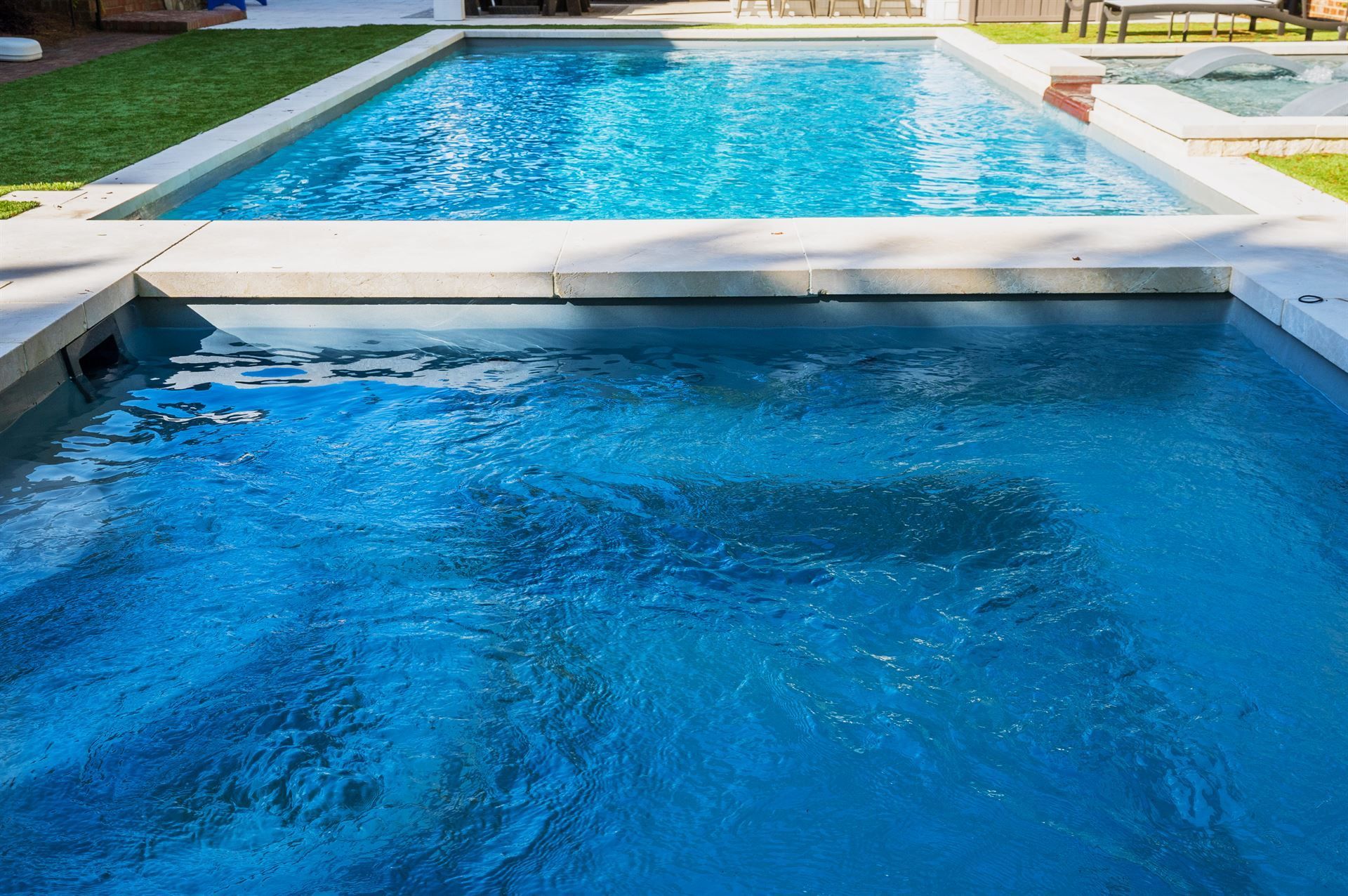 Blue swimming pool with a shallow lower section and a raised upper pool connected by a ledge