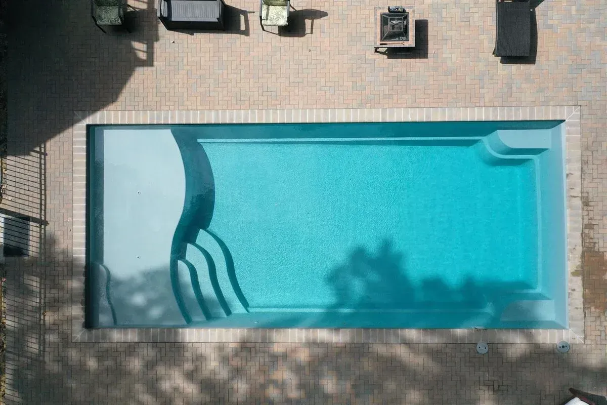Aerial view of a rectangular backyard swimming pool with blue water and patio furniture nearby