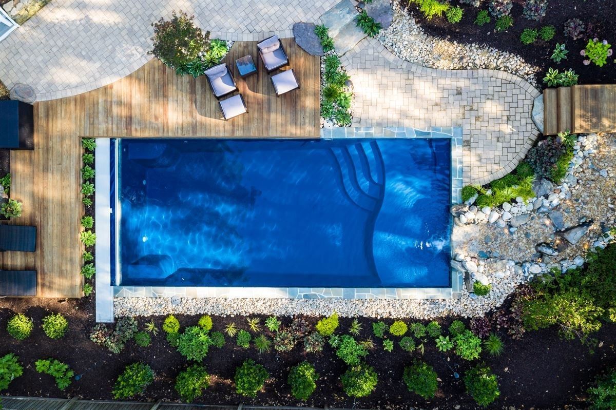 Overhead view of a backyard pool with patio seating, stone paths, and landscaped greenery
