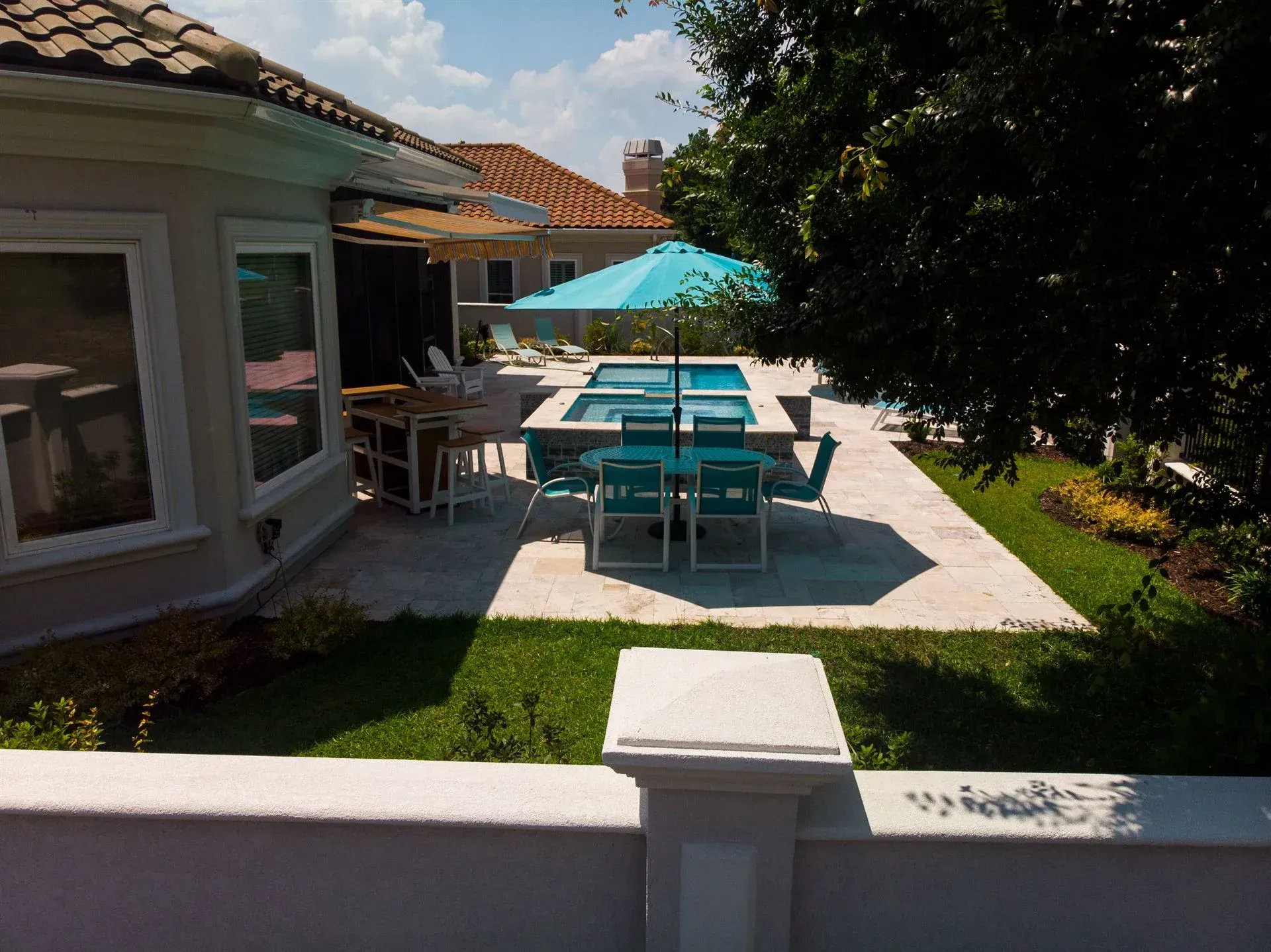 Backyard patio with turquoise table and chairs beside a house, under a blue umbrella