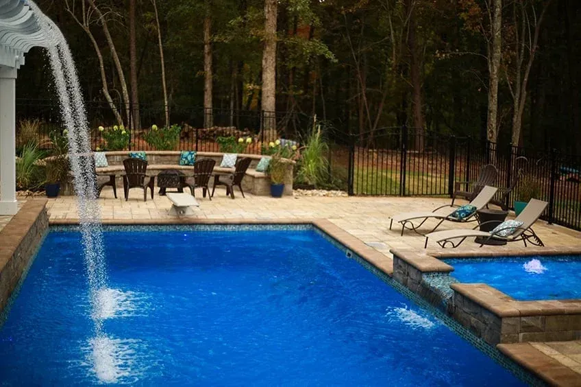 Backyard pool with waterfall, lounge chairs, and a hot tub surrounded by trees