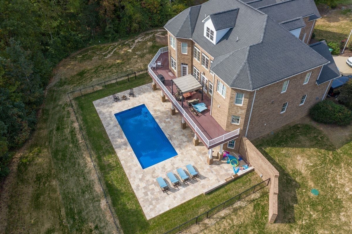 Aerial view of a brick house with a patio, blue pool, and lounge chairs in a fenced yard