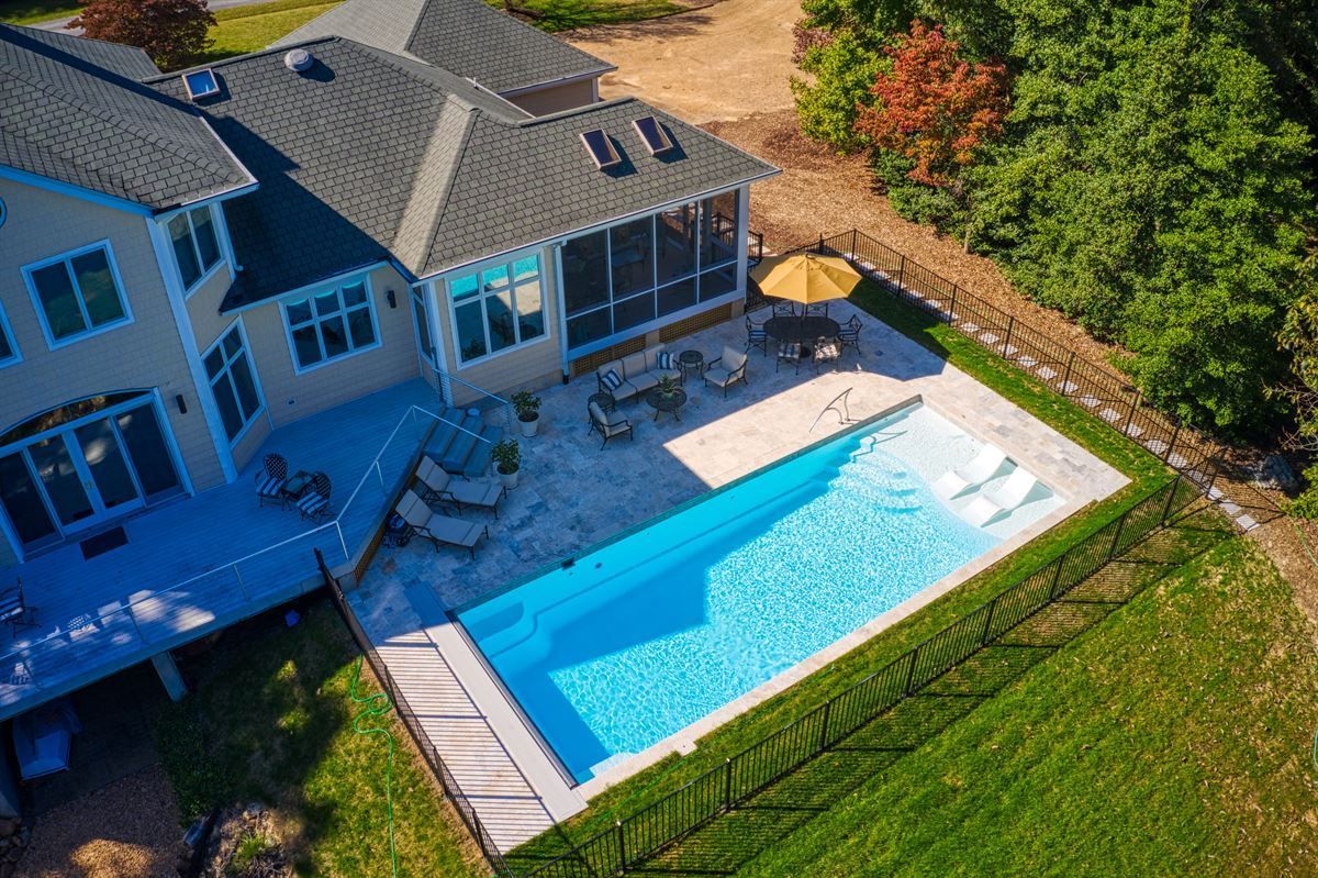 Aerial view of a house with a backyard patio and rectangular swimming pool beside a green lawn.