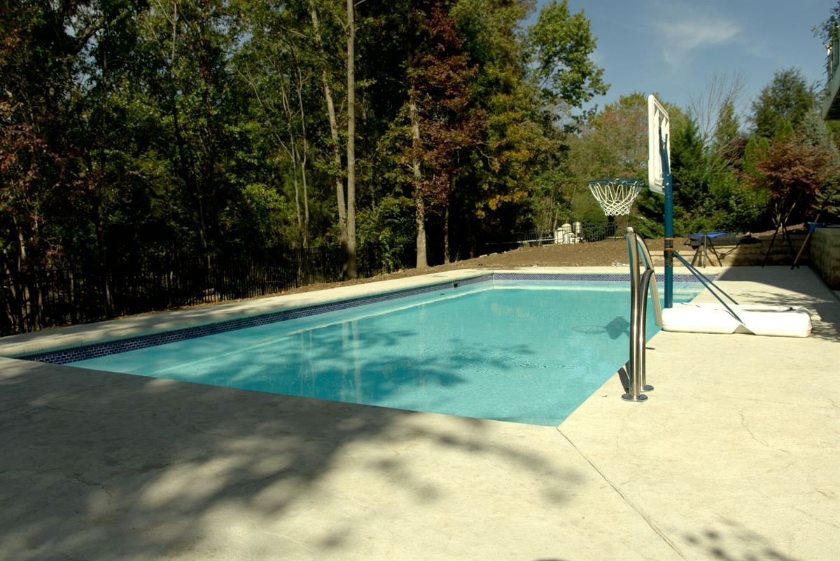 Outdoor swimming pool surrounded by trees, with a diving board and handrails on the deck.