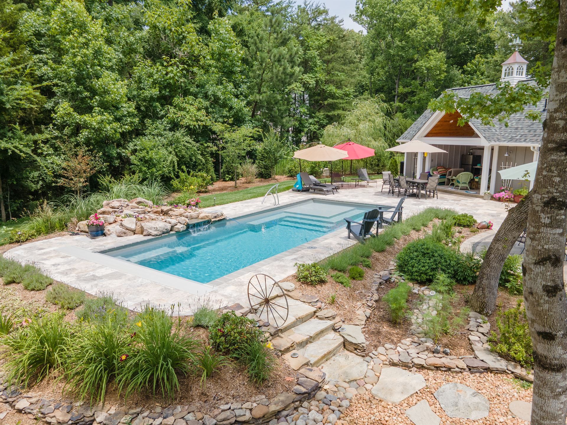 Backyard pool with patio, lounge chairs, umbrella, and lush greenery