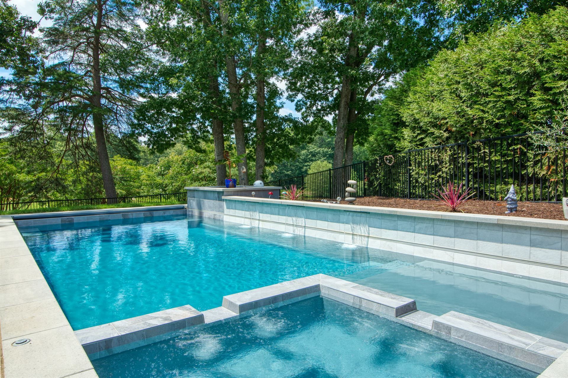 Backyard pool with blue water, hot tub, and stone patio surrounded by trees