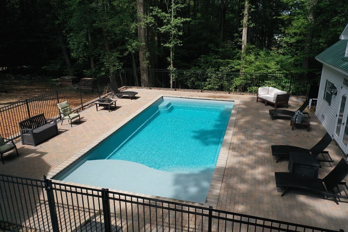 Rectangular backyard swimming pool with lounge chairs and a surrounding deck in a wooded setting