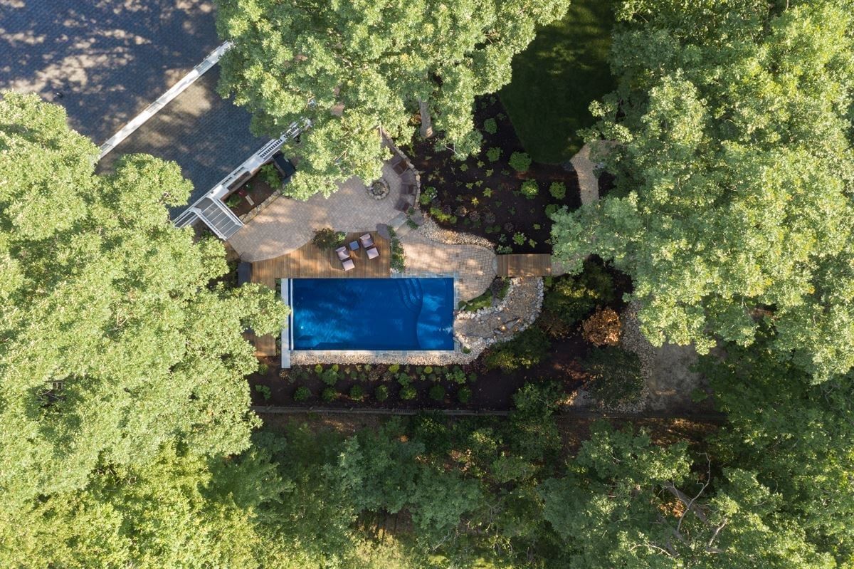 Aerial view of a backyard pool surrounded by trees and stone patio.