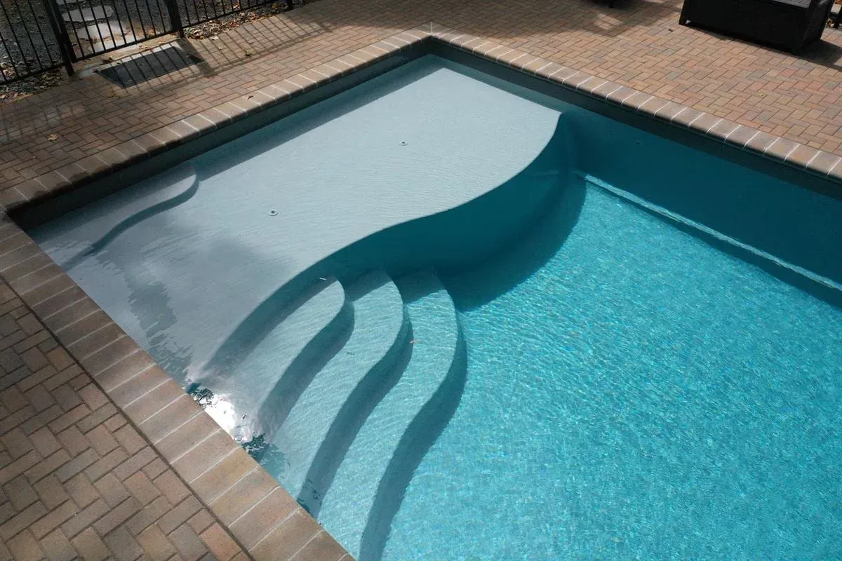 Blue swimming pool with curved steps and brick patio border.