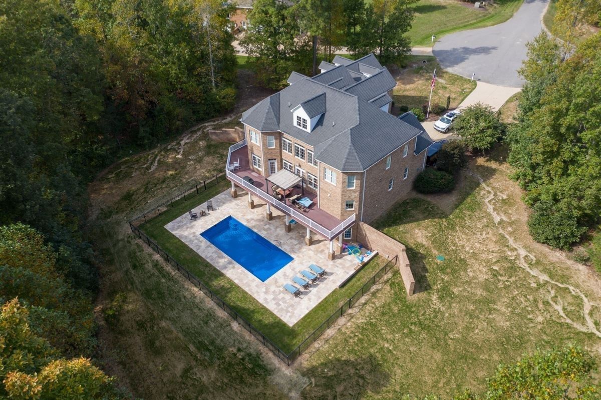 Aerial view of a house with a backyard pool and patio surrounded by grass and trees.