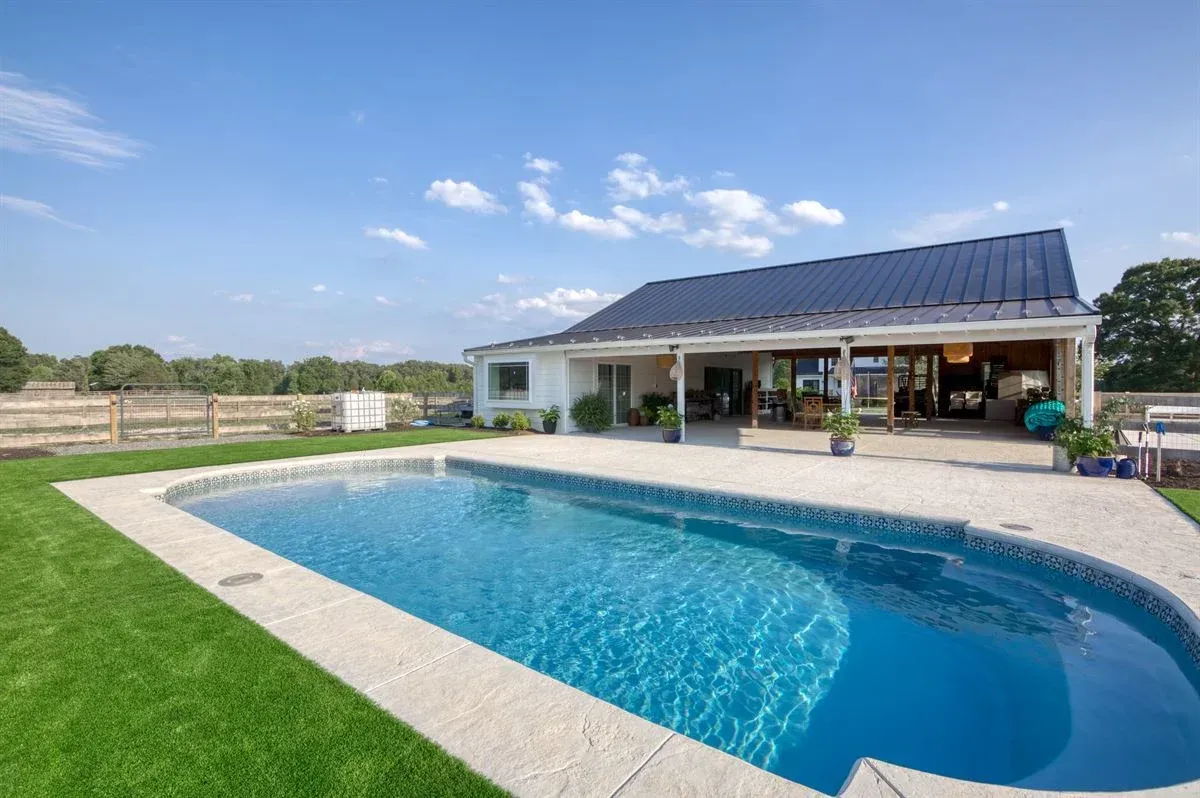 Backyard with a curved blue swimming pool beside a modern house under a clear sky