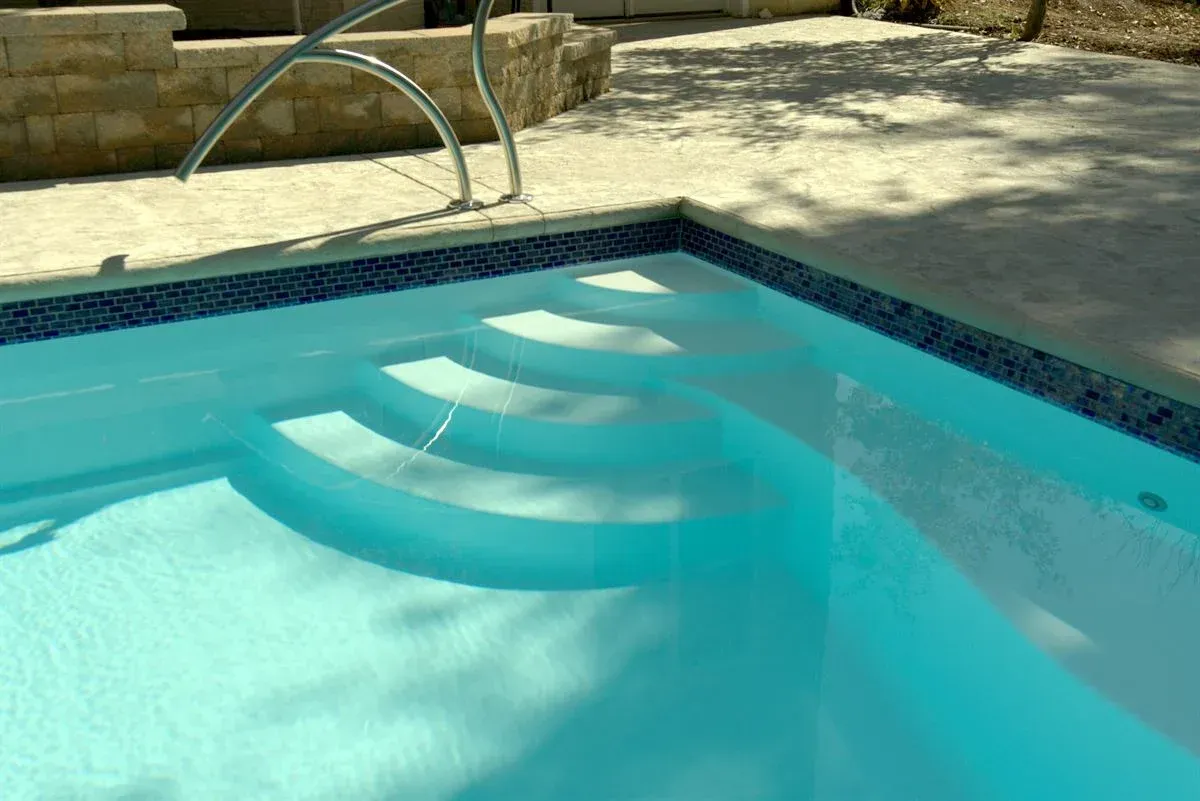 Swimming pool with light blue water and a submerged white pool ladder casting shadows